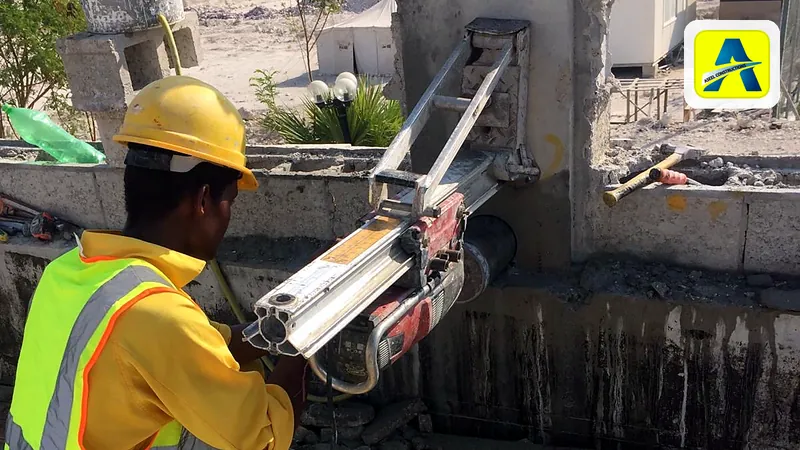 An Aseel worker in a hard hat runs a rig-mounted diamond core drill that bores horizontally into a concrete wall on an outdoor site